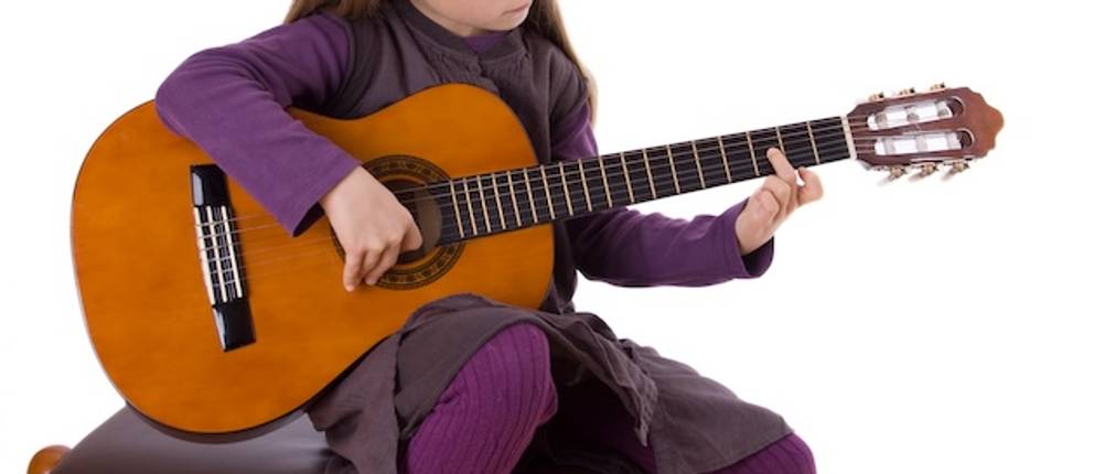 Fußbank für Gitarre im Test: Ein Mädchen in violetter Kleidung spielt im Sitzen auf einer braunen Gitarre.