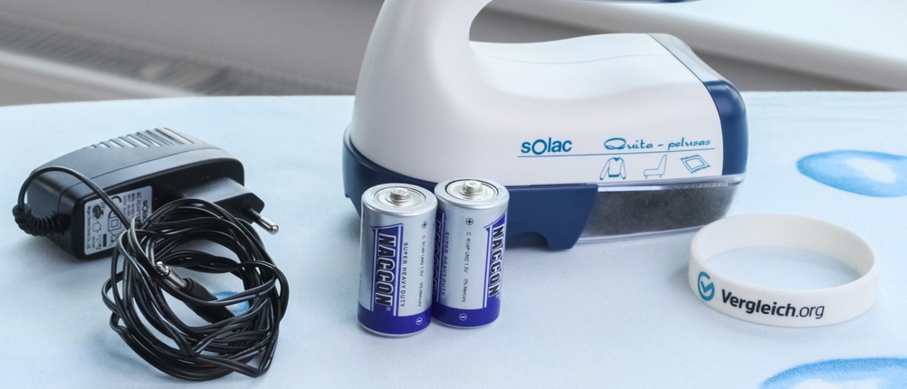 Netzteil, Batterien und Fusselrasierer von Solac auf einem Bügelbrett.