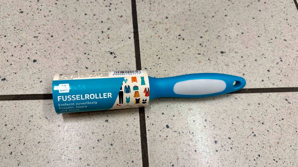Ein Fusselroller im Test liegt auf einem Fließenboden.
