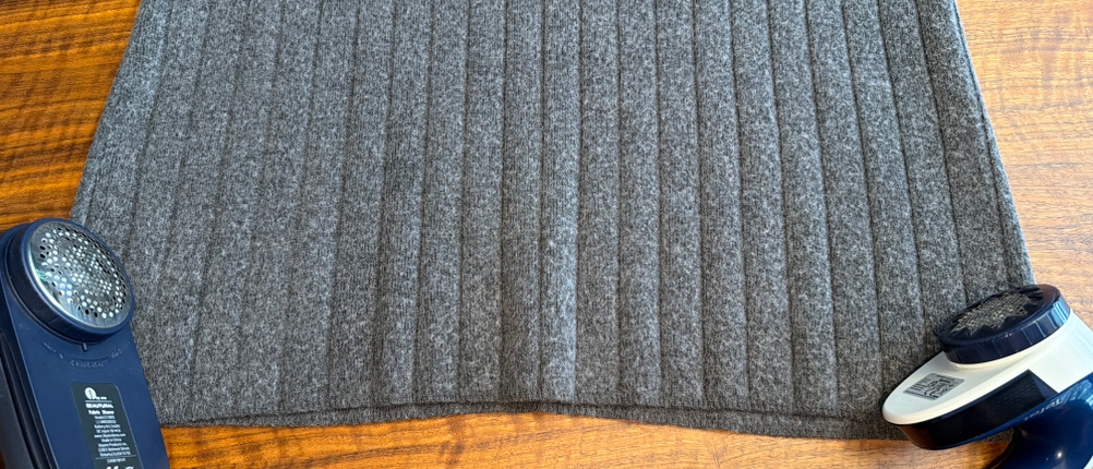 Links und rechts liegen jeweils Fusselrasierer von Philips und Tefal auf einem grauen Pullover.