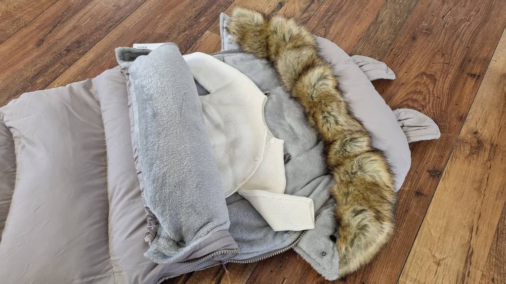 Fußsack halb geöffnet mit Babykleidungim Inneren.