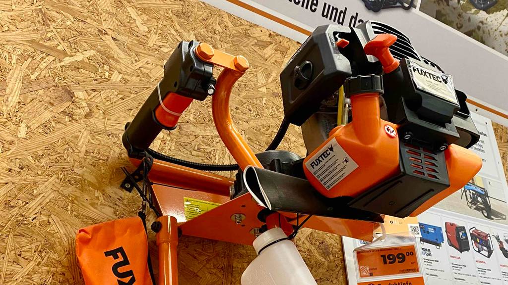 Nahaufnahme der Motoreinheit eines Fuxtec-Erdbohrers im Test: das orange-schwarze Modell ist mit verschiedenem Zubehör ausgestattet.