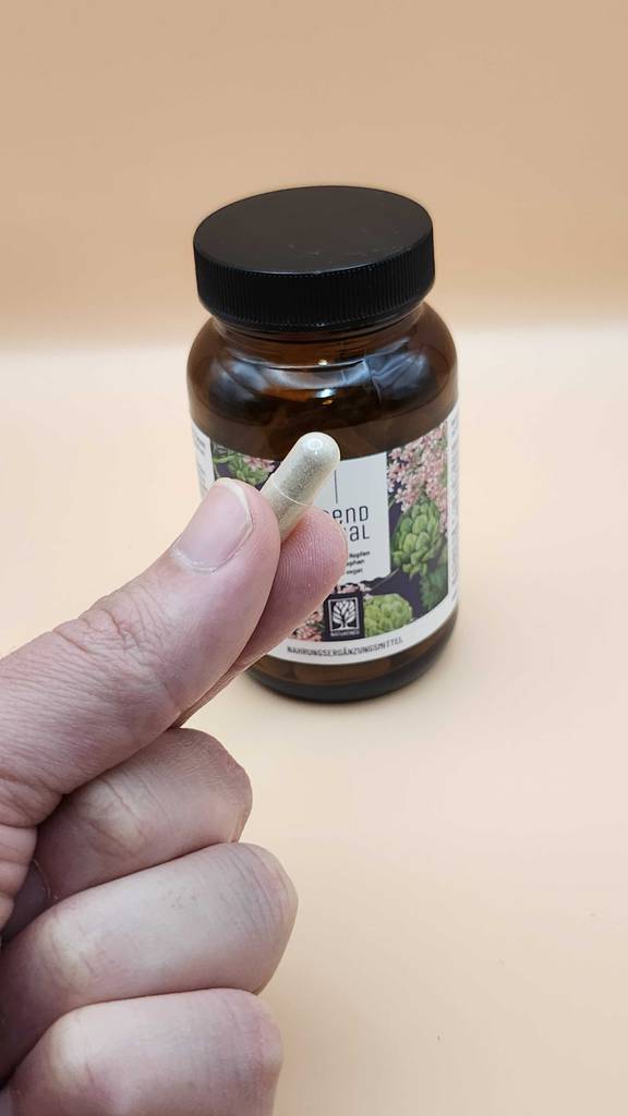 Gaba-Kapseln im Test: Eine Hand hält eine Kapsel zwischen den Fingern, im Hintergrund eine Flasche.