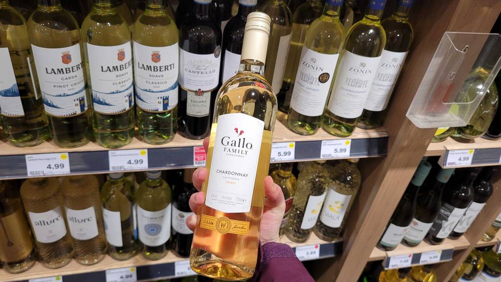 Eine Hand hält die Flasche mit getestetem Gallo-Wein vor einem Weinregal im Geschäft.