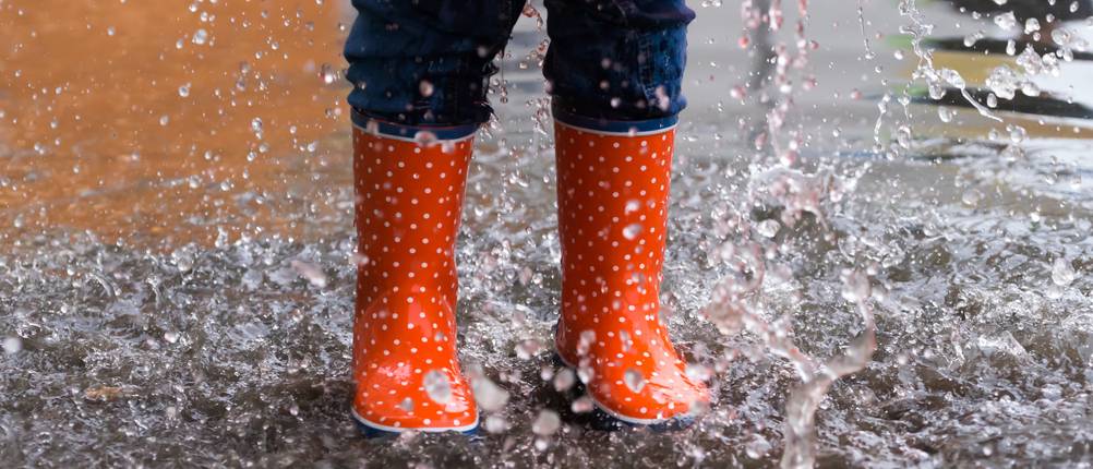 Gamaschen-Test: Kinderbeine in rot-weiß-gepunkteten Gummistiefeln, die Spaß im Regen haben
