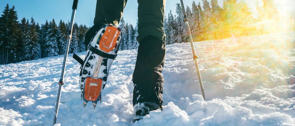 Gamaschen-Test: Winterwanderer, der mit Steigeisen und Stöcken durch tieferen Schnee läuft