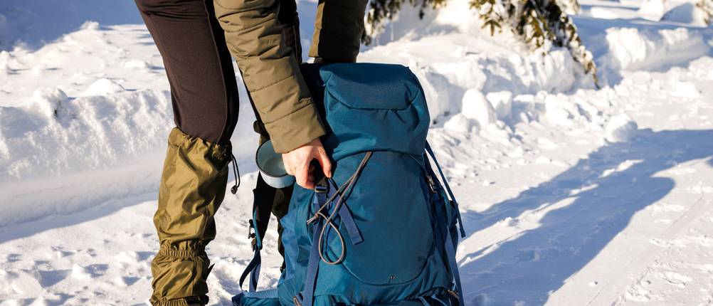 Gamaschen-Test: Frau beim Winterwandern, die sich über ihren Rucksack beugt, über ihren Wanderschuhen trägt sie Gamaschen