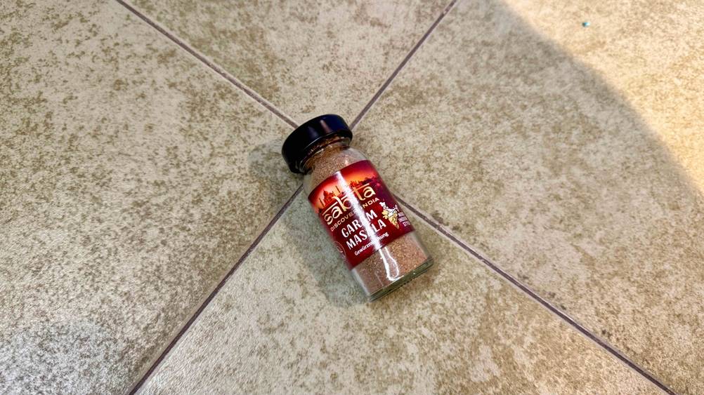 Ein Glas Garam Masala im Test auf einem Fließenboden liegend.