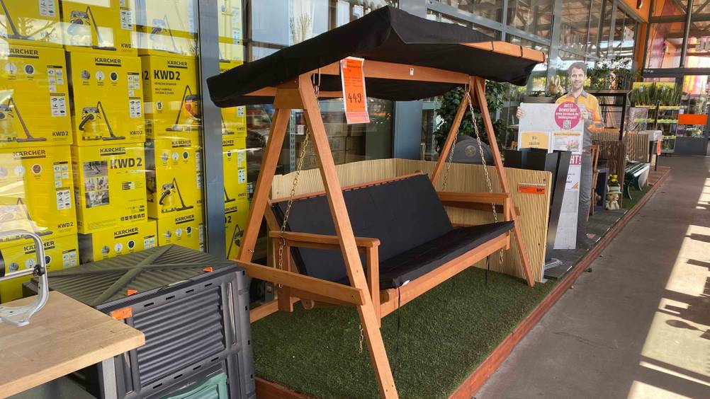 Hollywoodschaukel (Holz) getestet: Eine Schakel aufgebaut in einem Baumarkt zwischen anderen Produkten inklusive Preisangabe.