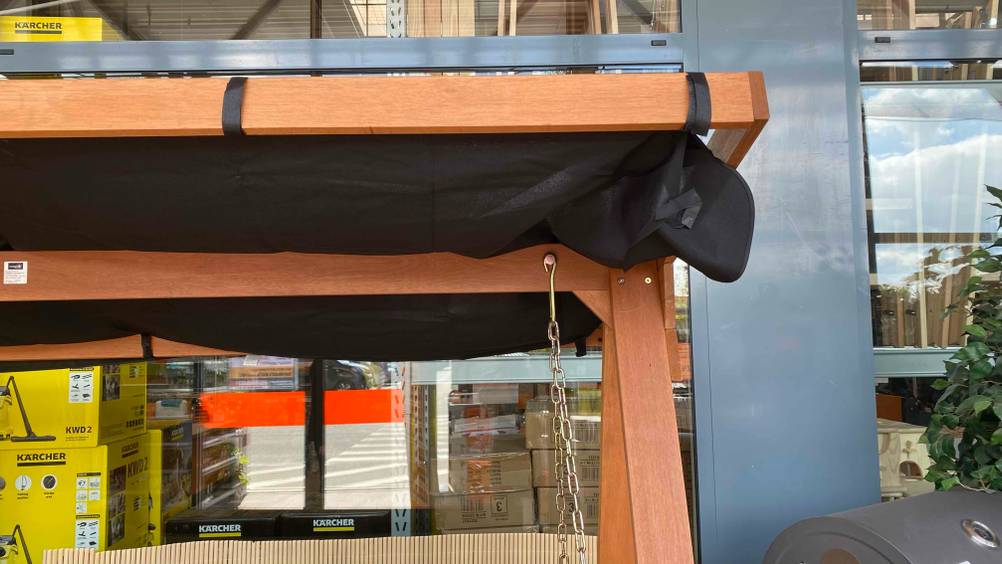 Nahaufnahme einer Ecke des Daches mit Stoff einer getesteten Hollywoodschaukel (Holz) vor einer Fensterwand.