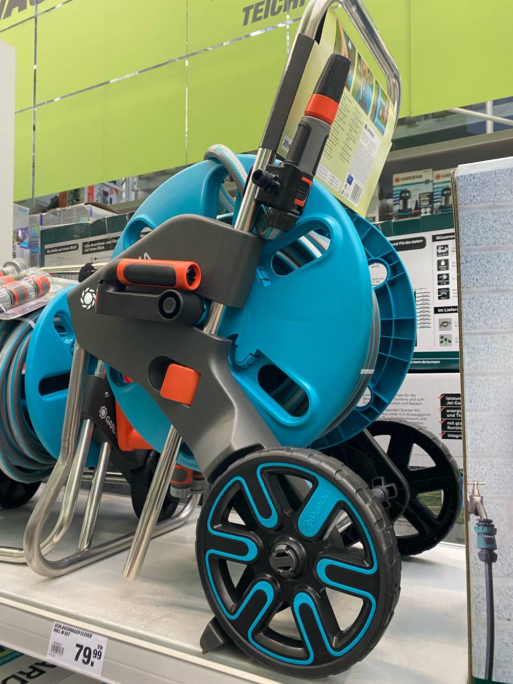 Schlauchwagen-3/4-Zoll-Test: Gesamtansicht eines türkisfarbenen Modells von Gardena inklusive Schlauch und ausziehbarem Griff auf einem Verkaufsregal.