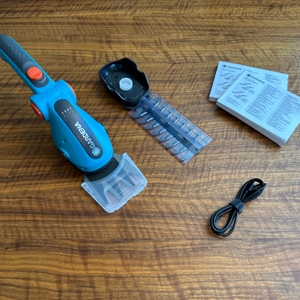 Der Lieferumfang der Gardena ComfortCut Li 9888-20 liegt auf einem Holztisch.