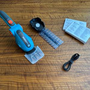 Der Lieferumfang der Gardena ComfortCut Li 9888-20 liegt auf einem Holztisch.