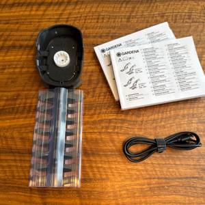 Das Zubehör der Gardena ComfortCut Li 9888-20 liegt auf einem Holztisch.