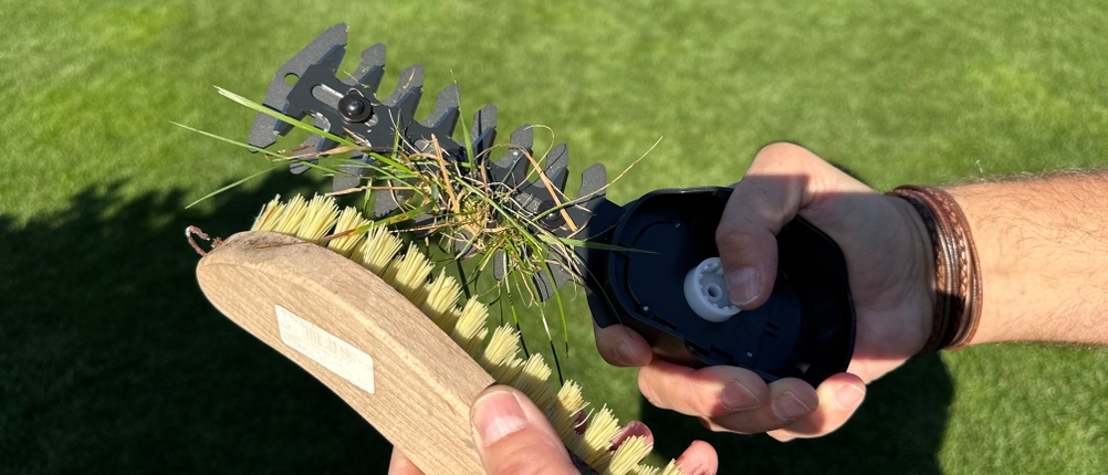 Mit einer Bürste werden Grasreste von der Gardena ComfortCut Li 9888-20 entfernt.
