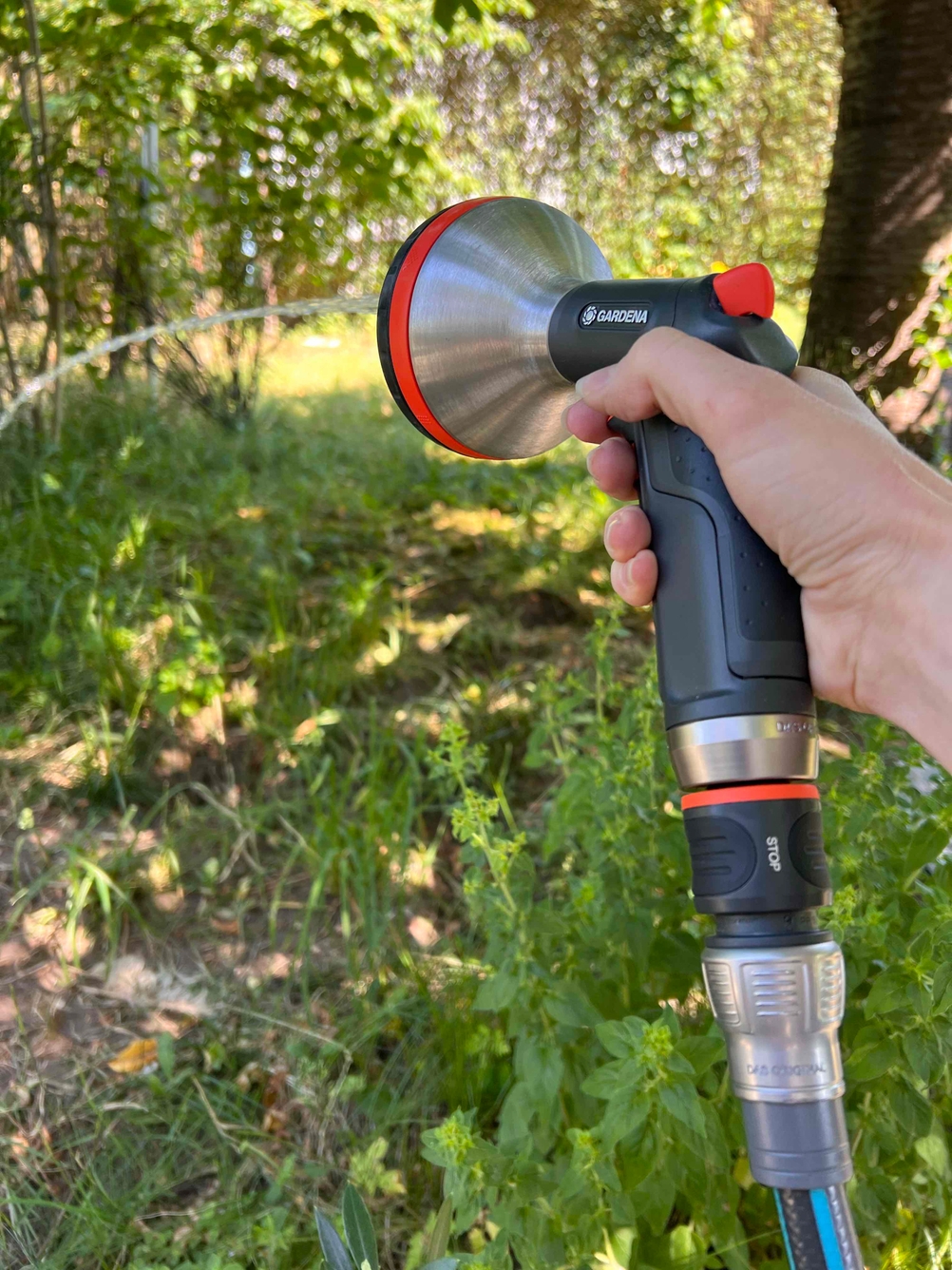 Gardena-Multibrause wird mit der Hand gehalten und sprüht Wasser in einen Garten