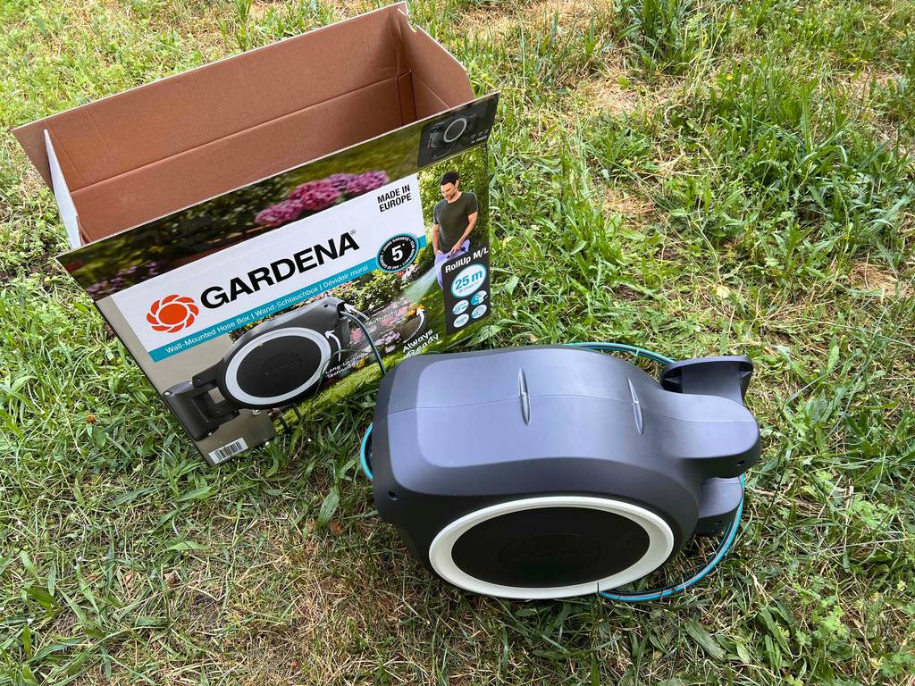 Ansicht von oben auf eine neben seiner offenen Verpackung auf Rasen stehende getestete Gardena-Schlauchbox.