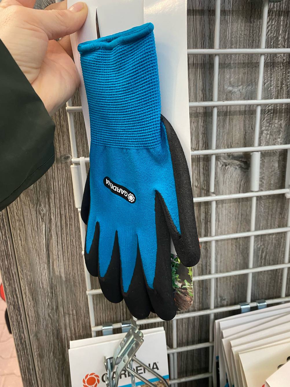 Hand greift nach blauen, getesteten Neopren-Handschuhen von Gardena in einem Verkaufsbereich