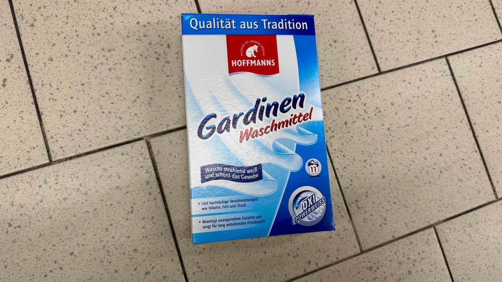 Auf dem Fließenboden liegt eine Packung des Gardinenwaschmittels im Test.