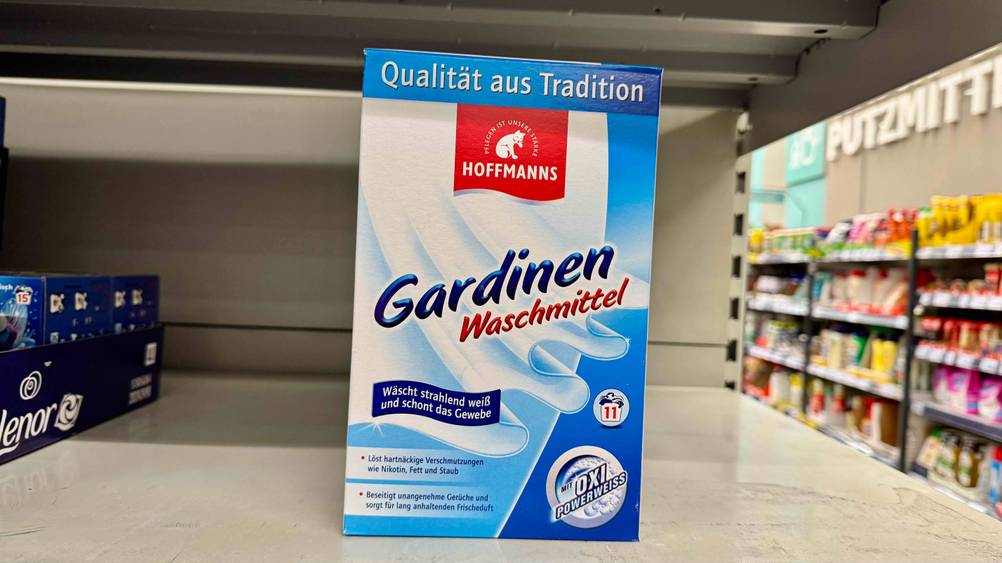 Auf einem hellen Regal steht eine Packung des getesteten Gardinenwaschmittels im Hintergrund der Laden mit Regalen.