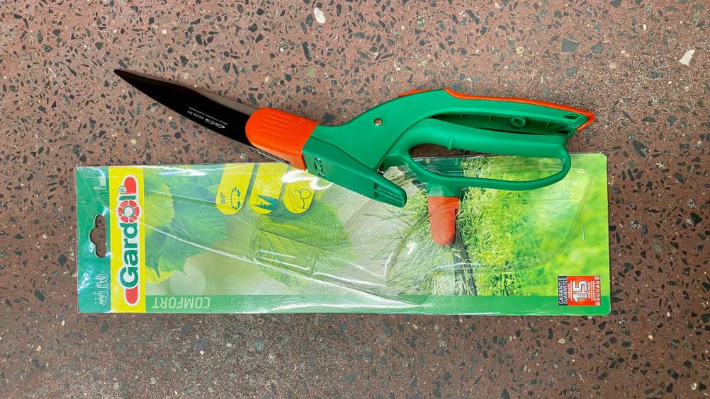 Eine getestete Grasschere liegt mit der Rückseite nach oben auf der Originalverpackung.