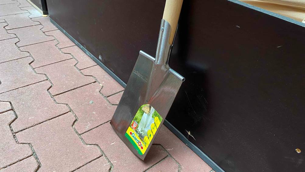 Nahaufnahme seitlich des Blattes eines Spatens im Test der an einer dunklen Fläche lehnt.