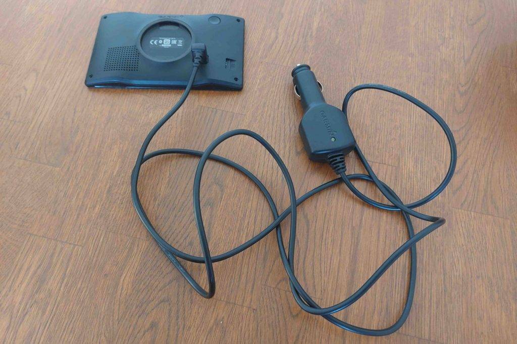 Im Test: Garmin Navi liegt mit Rückseite nach oben angeschlossen an ein 12V-Ladekabel angeschlossen auf einem Holzboden.