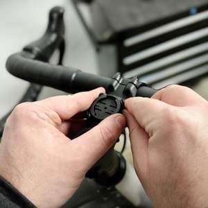 Zwei Hände montieren die Halterung des Garmin Edge Explore 2 an einem Fahrradlenker. Die Halterung wird mit einem Gummiband fixiert.