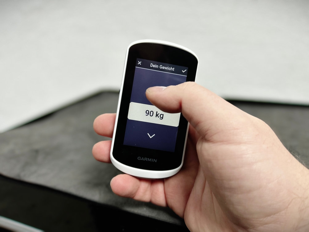 Ein Finger gibt im Garmin Edge Explore 2 ein Körpergewicht über den Touchscreen ein. Der Wert ist auf 90 kg eingestellt.