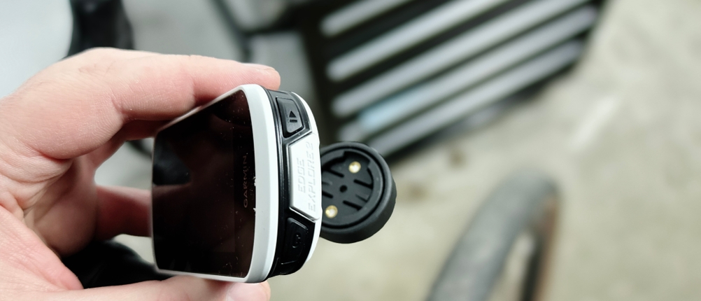 Eine Hand hält den Garmin Edge Explore 2 mit geöffneter Schutzkappe am Ladeanschluss. Die Anschlüsse sind gut sichtbar.