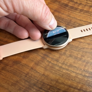 Eine Hand zieht eine Folie von der Garmin Vivoactive 6