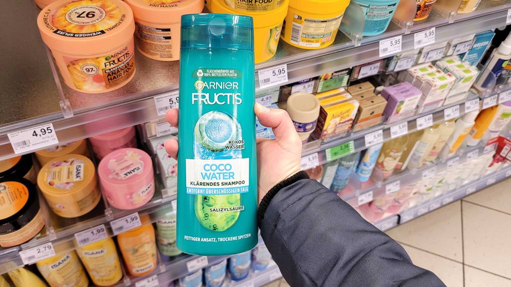 Eine Hand hält eine grüne Quetschflasche mit Fructis-Shampoo im Test vor einem Regal im Drogeriemarkt.
