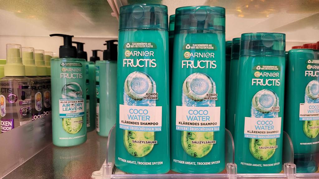 Mehrere grüne Quetschflaschen mit getestetem Fructis-Shampoo stehen auf einem Regal im Drogeriemarkt.