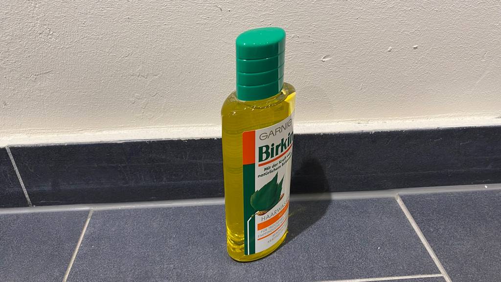 Eine Flasche mit grünem Schraubverschluss und getestetem Haarwasser von Garnier steht auf einem grauen Boden.