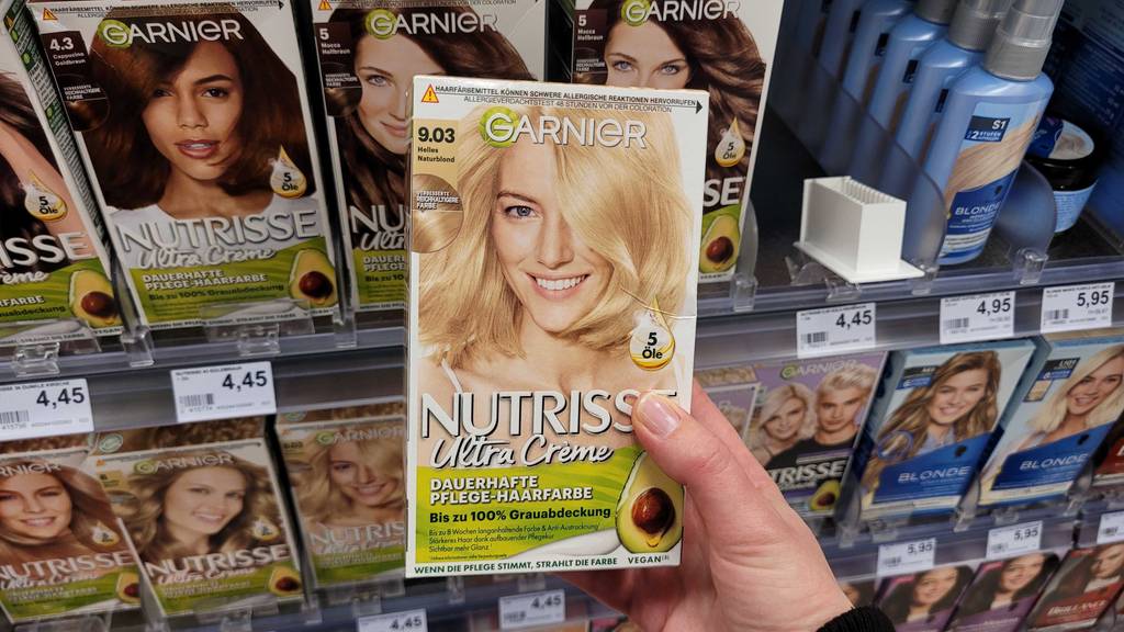Im Test: Eine Hand hält eine Packung Haarfärbemittel blond vor einem Regal mit Haarfarben.