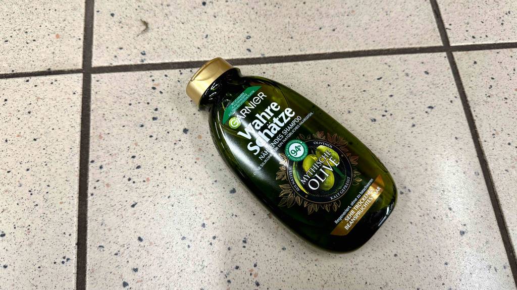 Im Test: Olivenöl-Shampoo der Marke Garnier in der Quetschflasche liegt auf einem Fliesenbelag.