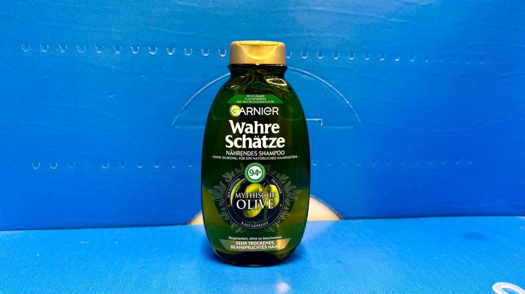 Eine Quetschflasche mit getestetem Olivenöl-Shampoo steht vor einem blauen Hintergrund.