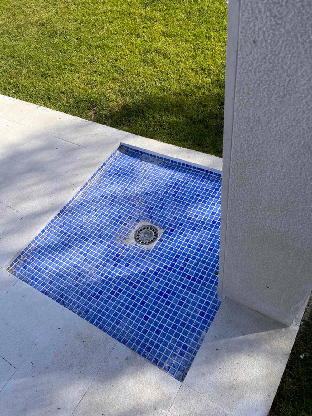 Nahaufnahme des mit Mosaik-Fliesen ausgelegten Ablaufbereichs einer getesteten Gartendusche im Außenbereich.