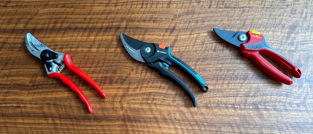 Drei Gartenscheren liegen nebeneinander auf einem Holztisch