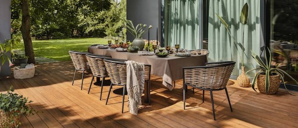 Getesteter Gartentisch mit Stühlen mit grauer Tischdecke und Stühlen im Rattandesign auf einer Holzterrasse.