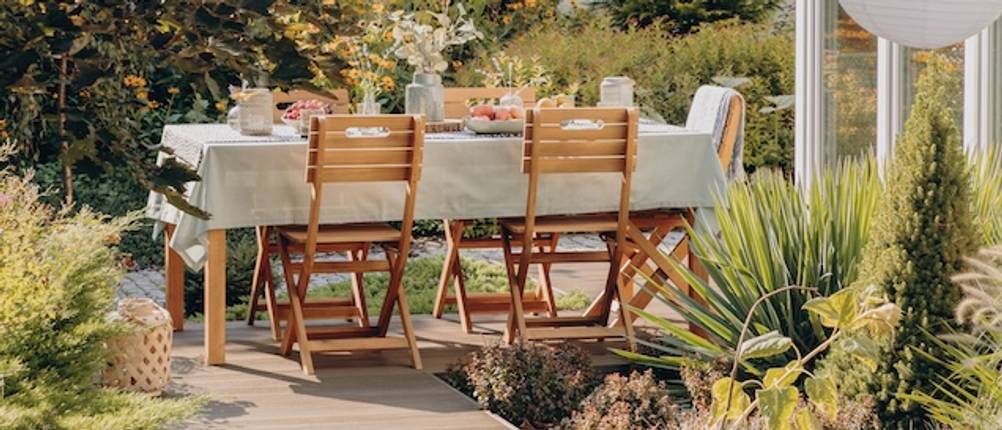 Gartentisch mit Stühlen getestet: Ein rechteckiger Gartentisch mit einer weißen Tischdecke und klappbaren Holzstühlen.