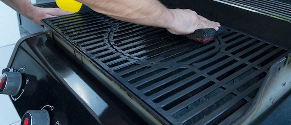 Getesteter Gasgrill in Schwarz dessen Grillrost von einer Männerhand gereinigt wird.