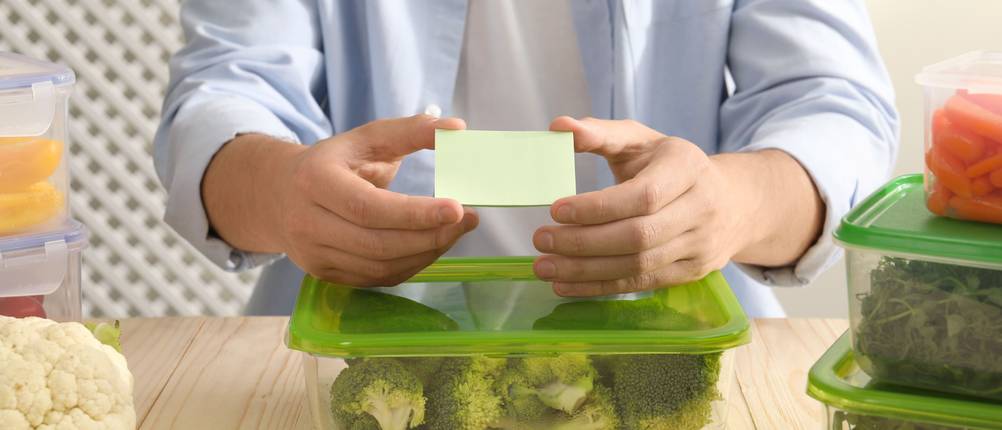 Gefrieretiketten-Test: Mann hält Aufkleber über eine Frischhaltedose mit Brokkoli
