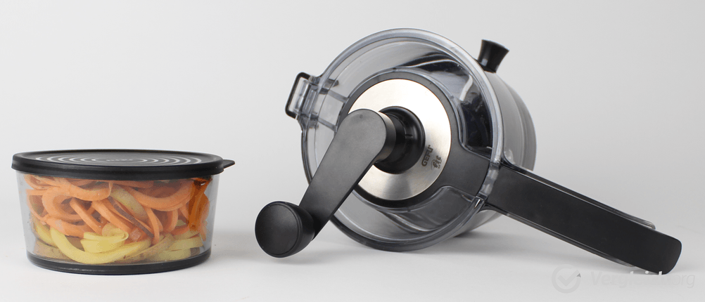 Ein Spiralschneider liegt neben einer Plastikdose, die mit Gemüsespiralen gefüllt ist.