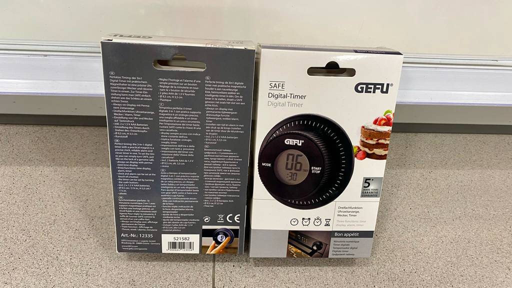 Zwei verpackte digitale Timer von Gefu befinden sich für den Test bereit auf dem Boden. Ansicht auf Vorder- und Rückseite mit Beschriftung.