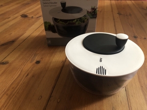 Salatschleuder steht vor einem Karton auf einem braunen Holztisch