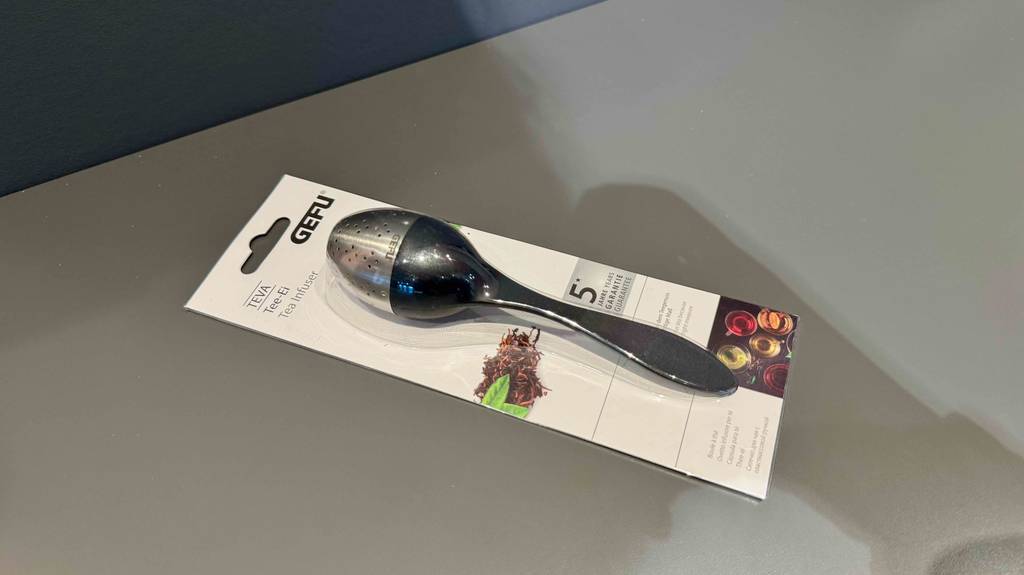 Im Test: Ein Tee-Ei im Löffeldesign liegt innerhalb seiner Verpackung auf einem grauen Regalboden.