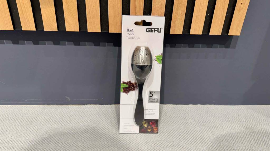 Tee-Ei-Test: Ein Modell im Löffeldesign lehnt inklusive Verpackung an einer grauen Wand.