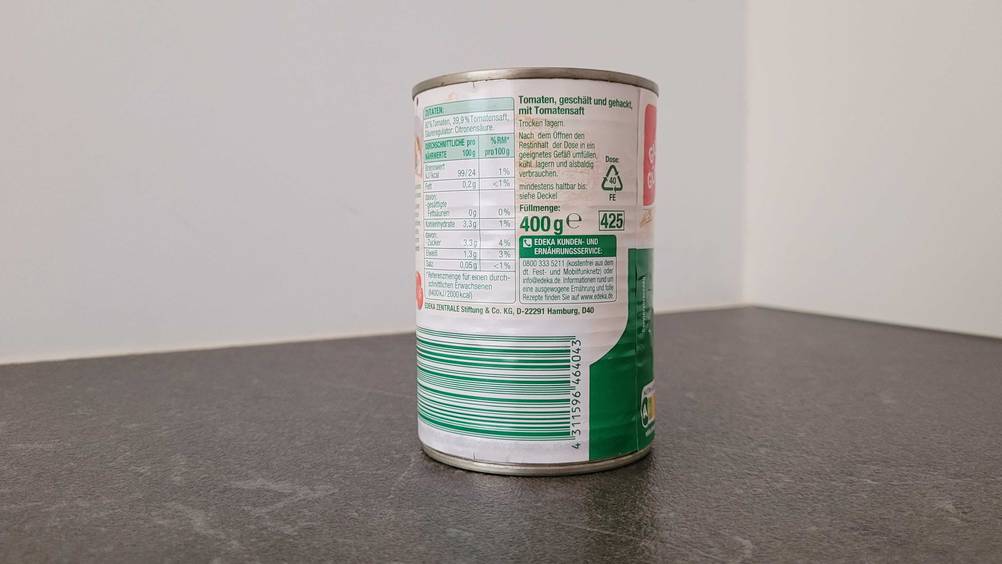 Gehackte Tomaten getestet: Rückseite der Dose mit Informationen auf einer dunklen Fläche vor einer hellen Wand.