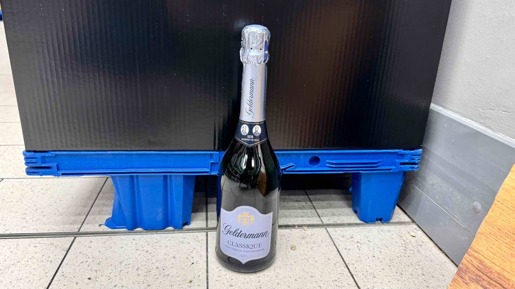 Eine Flasche des getesteten Geldermann-Sekts steht vor einer blauen Palette auf dem Boden.
